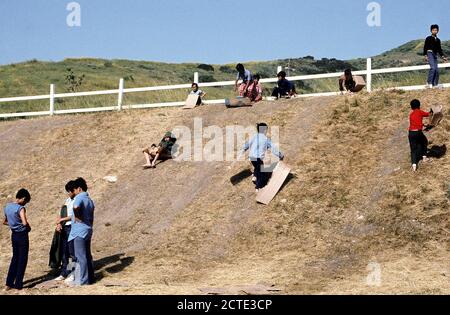 1975 - Bambini scorrere su una collina a una temporanea struttura alloggiativa per rifugiati vietnamiti. Foto Stock