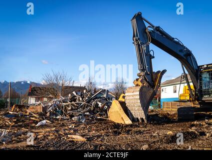 Bulldozer da demolizione davanti alle macerie dell'edificio. Benna abbassata, vista laterale. Macchina da costruzione gialla con edifici residenziali e montagne. Foto Stock