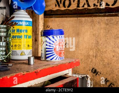 Scenario d'officina con tavolo/panca rosso, latta lucidante in metallo (Brasso), clacson ad aria di segnalazione e contenitore con smalls. Focus su metallo può legno morbido sfondo. Foto Stock