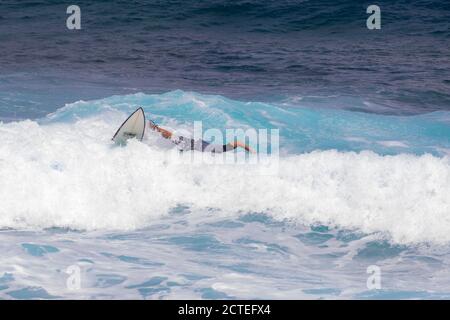 Capretto surfer che cade fuori dell'onda a Maui, Hawaii. Bambini hawaiani che pulono il surf. Wipeout dilettante del surfer. Surfista in camicia grigia cade dalla tavola da surf. Foto Stock