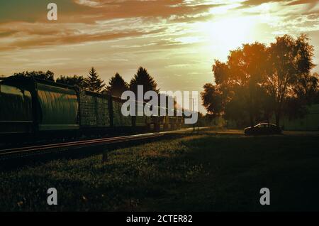 Maple Park, Illinois, Stati Uniti. Un treno merci Union Pacific Railroad si dirige verso il sole tramontante mentre un veicolo soleggiato attende un passaggio di classe. Foto Stock
