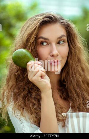 Donna in camicia bianca che tiene in mano l'avocado Foto Stock