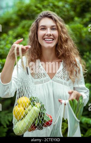 Donna in abito bianco che tiene borse con verdure diverse Foto Stock