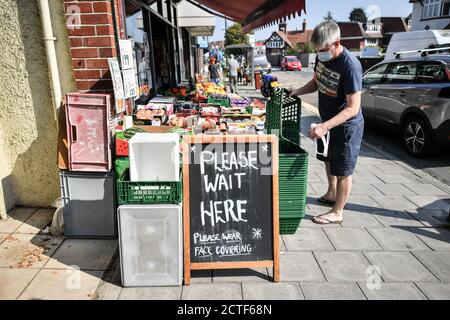 Il volto che cambia della strada alta. Segnaletica all'esterno di un fruttivendolo che consiglia agli acquirenti di indossare rivestimenti per il viso, sulla High Street di Henleaze, Bristol, circa sei mesi dopo la sera del marzo 23, quando il primo ministro Boris Johnson ha annunciato restrizioni a livello nazionale. Foto Stock