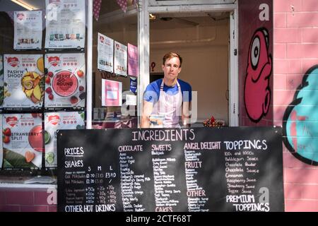 Il volto che cambia della strada alta. Il proprietario del negozio Shake Express Smoothie Chris Horsley si trova dietro il suo menu board, che usa per impedire ai clienti di entrare nel suo negozio e mantenere la distanza sociale, su North Street a Bedminster, Bristol, a circa sei mesi dalla sera del 23 marzo, quando il primo ministro Boris Johnson ha annunciato restrizioni a livello nazionale. Foto Stock