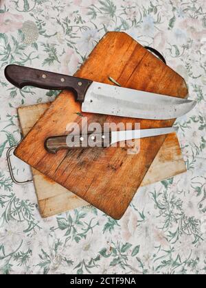 tagliere in legno con coltelli da cucina, posto su una vecchia tovaglia di fiori, fotografia con vista dall'alto Foto Stock