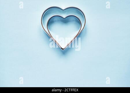 Due frese per biscotti in metallo a forma di cuore su blu chiaro sfondo con spazio di copia Foto Stock