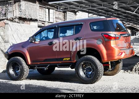 Vista laterale isolata di una nuova auto Isuzu MUX SUV dai colori maroon con ruote grandi, fotografata in un quartiere più povero, Filippine, Asia Foto Stock