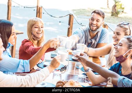 Felice giovane donna che indossa la maschera sorridente alla macchina fotografica al bar del ristorante. Gruppo di amici multirazziali che hanno una conversazione divertente e che parlano t Foto Stock