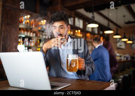 Uomo che beve birra e fuma sigaretta mentre lavora sul computer. Cattivo concetto di abitudine. Foto Stock