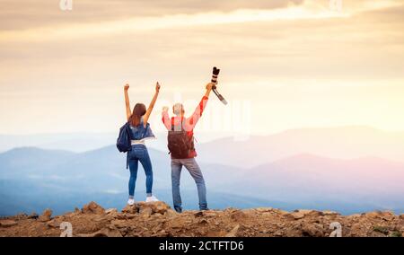 La coppia dei viaggiatori felici ha conquistato la cima della montagna, solleva le mani con la macchina fotografica e scatta foto dei paesaggi durante il viaggio Foto Stock