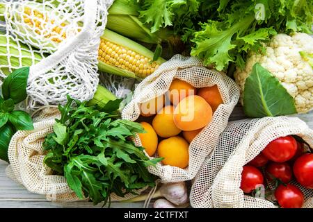 Frutta fresca e verdura in sacchetti di cotone eco sul tavolo in cucina. Mais, albicocche, pomodori, rucola, insalata di mercato. Zero rifiuti shopping con Foto Stock