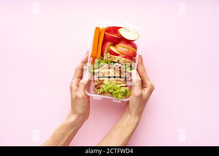 Donna che tiene una scuola pranzo vista dall'alto. Pasto nutriente sano in contenitore dall'alto con spazio di copia su sfondo rosa Foto Stock