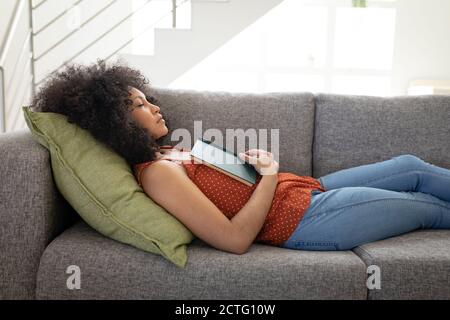 Donna con libro dormendo sul divano a casa Foto Stock