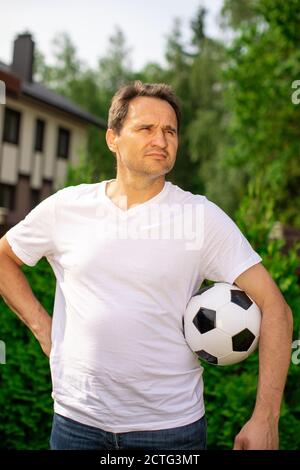 L'uomo bello dell'adulto tiene la sfera di calcio in piedi all'aperto, giocatore dilettante di calcio Foto Stock