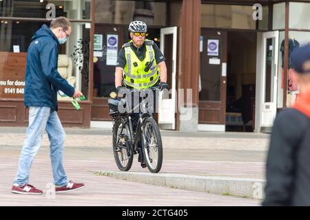 Un poliziotto è avvistato sulla High Street dal centro della città di Paisley, che, comprese altre città del Renfrewshire, ha avuto ulteriori misure di blocco aggiunto a mezzanotte la scorsa notte. A causa di un picco nei casi di Covid-19. Credito: Euan Cherry Foto Stock