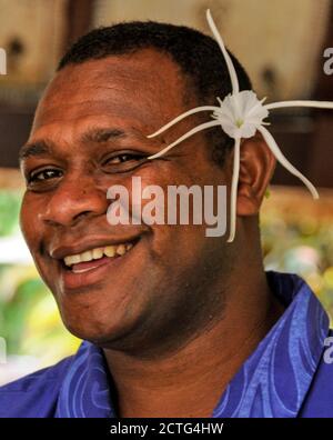 Un membro del personale dell'hotel delle Fiji che indossa un giglio bianco comune - un fiore nativo delle Fiji nel Sud Pacifico. Foto Stock