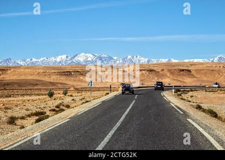 Vista panoramica di una strada sul deserto contro la montagna innevata dell'atlante e un cielo limpido, Ouarzazate Marocco Foto Stock