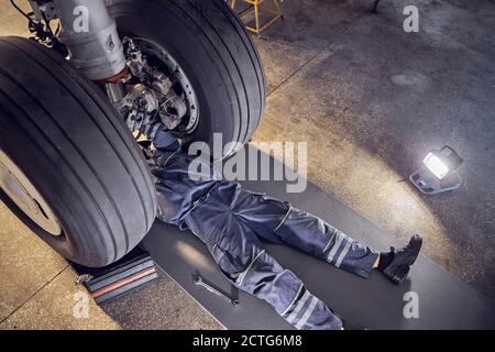 Vista dall'alto del ritratto di un ingegnere aeronautico su cui è in corso una certa manutenzione un equipaggiamento di atterraggio di un grande aeromobile in un servizio hangar Foto Stock