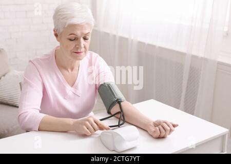 Signora anziana con ipertensione che misura la pressione sanguigna lei stessa Foto Stock