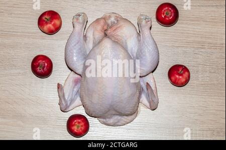 Un primo piano di un pollo intero con mele rosse intorno su sfondo di legno. Isolato. Ripieno di pollo con mele rosse. Foto Stock