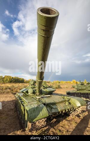 Un colpo ad alto angolo del carro armato russo T-64 nel campo. Cannone rivolto verso l'alto direttamente nella fotocamera. Cielo blu nuvoloso come sfondo. Foto Stock