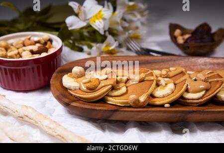 Frittelle con mix di noci e burro di arachidi su sfondo bianco con fiori. Cibo alla moda. Foto Stock