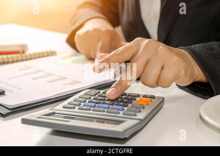 Primo piano di uomini d'affari o contabili che tengono una penna per premere sulla calcolatrice e luce vicino alla finestra. Calcoli concettuali, informazioni aziendali Foto Stock