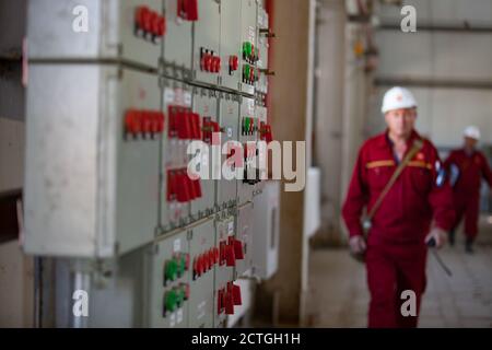 Quadro di comando remoto per apparecchiature elettriche e di elaborazione (console). Raffineria di petrolio e impianto di lavorazione del gas. Operai di raffineria offuscati in casco bianco. Foto Stock