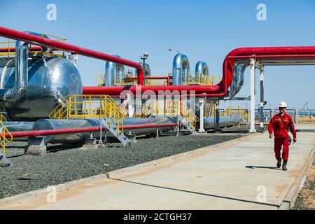 Regione di Aktobe/Kazakhstan - Maggio 04 2012: Stabilimento di raffinazione del petrolio. Operaio asiatico in abbigliamento da lavoro rosso e casco bianco con radio set su scambiatori di calore Foto Stock