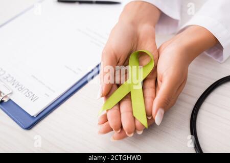 vista dall'alto del medico che tiene il nastro di consapevolezza verde vicino alla forma di reclamo di assicurazione, concetto di salute mentale Foto Stock