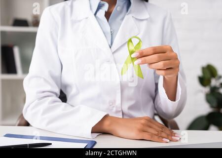 vista parziale del medico che tiene il nastro di consapevolezza verde, concetto di salute mentale Foto Stock