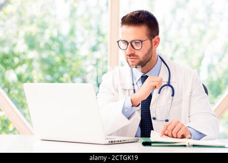 Un medico di pensiero seduto dietro il computer portatile mentre lavora in ufficio medico. Foto Stock