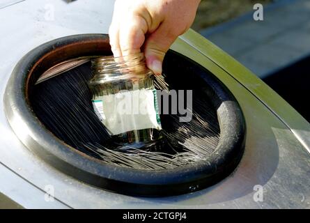 Un uomo che fa cadere il vaso di vetro vuoto nel contenitore per la separazione dei rifiuti domestici. Un segno di consapevolezza in materia di ambiente, gestione dei rifiuti e clima. Foto Stock