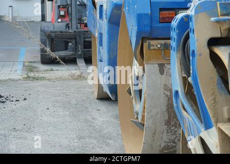 Attrezzature di ingegneria pesante, tra cui rullo di separazione del tamburo dell'asfaltatrice blu e impilatore per carrelli elevatori rosso e nero parcheggiato durante i giorni del fine settimana vicino alla costruzione. Foto Stock