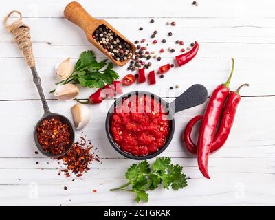 salsa rossa piccante al pepe, ingredienti, spezie su una superficie di legno bianco Foto Stock