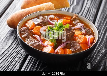 Ragù di manzo Bo Kho in salsa piccante con carote servite con pane vietnamita da vicino in un recipiente sul tavolo. Orizzontale Foto Stock