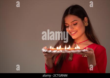 Donna in abbigliamento etnico guardando un piatto pieno di diya in mano Foto Stock