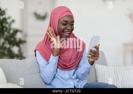 Comunicazione durante la quarantena. Donna musulmana con videochiamata su smartphone a casa Foto Stock