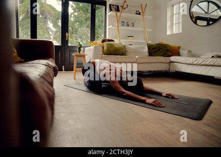 Vista laterale della giovane donna africana che fa l'esercitazione di idoneità a. casa su tappetino yoga Foto Stock