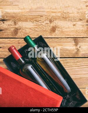 Bottiglie di vino rosso e bianco in una scatola su sfondo di legno, vista dall'alto. Confezione regalo, festa, modello di invito Foto Stock