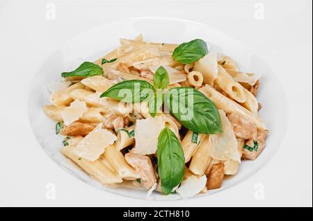 Porzione di pasta cotta di cucina italiana con pezzi di pollo fritti, fette di parmigiano, decorata con basilico isolato su piatto bianco Foto Stock