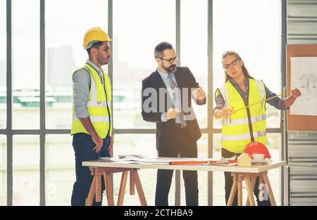 Team di architetti multietnici che lavorano ai piani di costruzione nella sala riunioni. Gli ingegneri discutono sul progetto in ufficio. Uomo d'affari maturo e donna Foto Stock