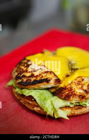 Hamburger di pollo con formaggio cheddar fuso cotto alla griglia American diner cafe.Hamburger preparazione sandwich in cucina fast food ristorante Foto Stock