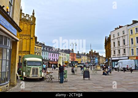 Le persone che passeggiano attraverso il Cirencester Market Place, con un vecchio van Citroen HY francese in uso come una stalla di caffè. Chiesa di San Giovanni Battista alle spalle. Foto Stock