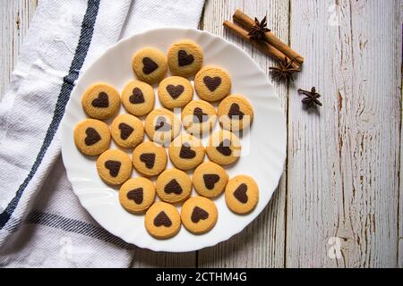 Vista dall'alto dei biscotti a forma di cuore al cioccolato in bianco piatto e dolci alla cannella su sfondo Foto Stock