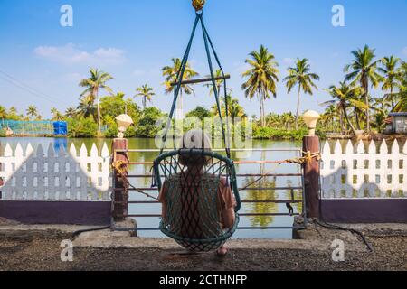 India, Kerala, Kollam, Resort sull'isola di Munroe, turista in sedia pensile che guarda alle acque posteriori Foto Stock