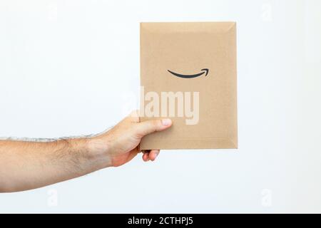 La mano di un uomo tiene una busta di carta Amazon su sfondo bianco. Consegna espressa. Il corriere ha portato il pacco Foto Stock