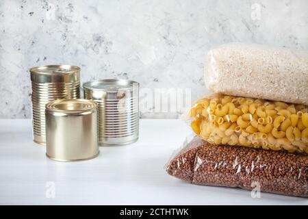 assistenza umanitaria a favore di famiglie povere e grandi. Donazione durante la crisi. Lattine di stagno, cibo in scatola, stufato, grano saraceno, riso, pasta in sacchetti trasparenti Foto Stock