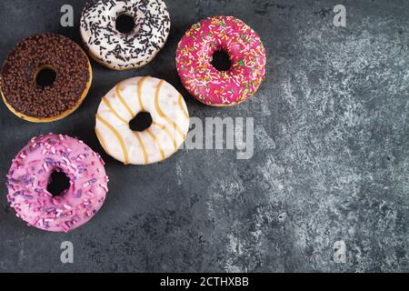 Ciambelle dolci e deliziose al forno con briciola di pasticceria su fondo di cemento grigio. Buon giorno di Donut. Poster del giorno nazionale delle ciambelle. Cibo americano di delicatezza Foto Stock